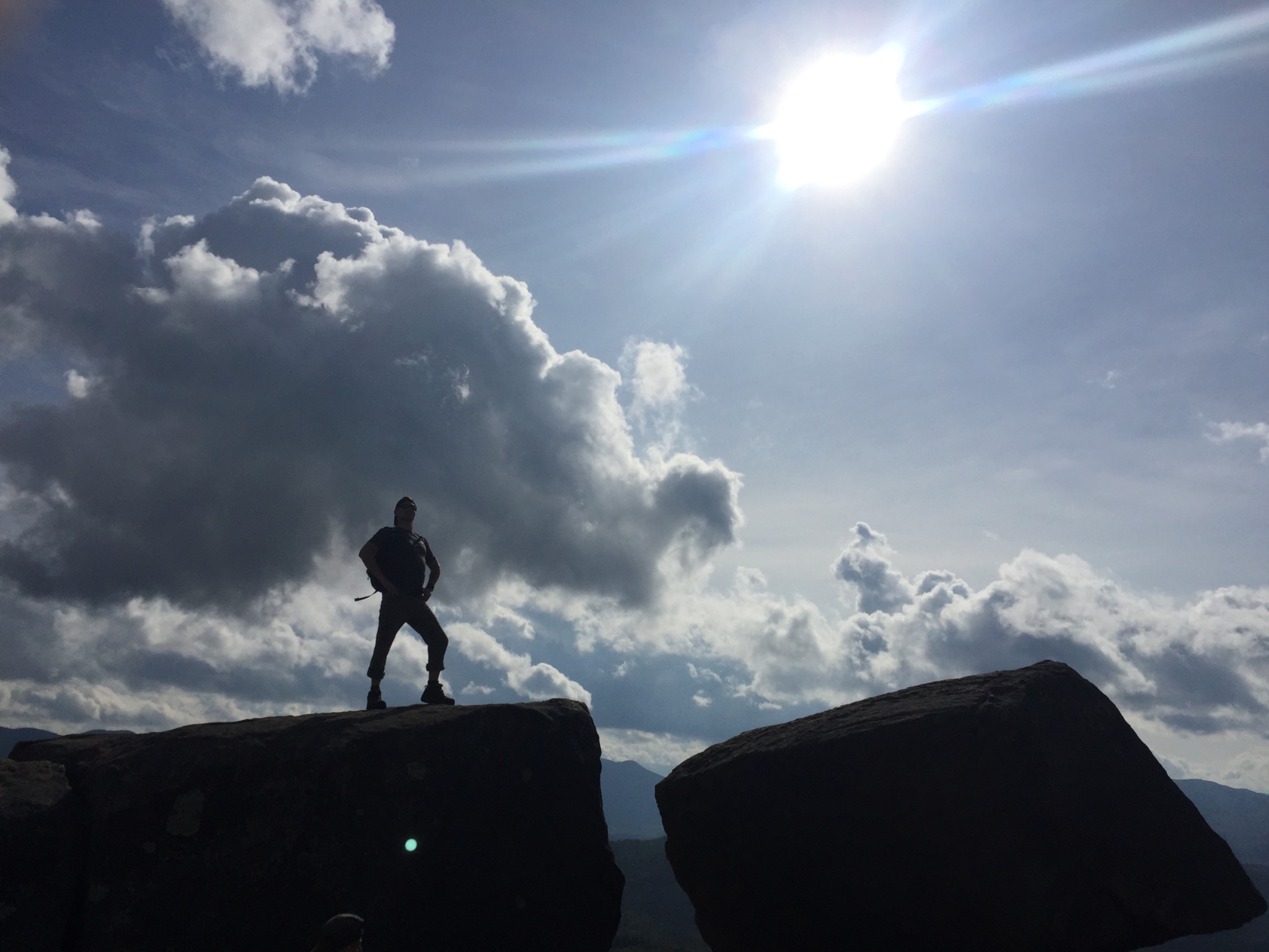Hiker standing on a rocky overlook under a bright Hudson Valley sky